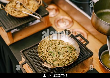 A close-up of a frying pan with spaghetti on a cast iron stove in the kitchen during cooking. Stock Photo