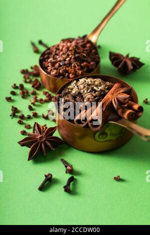 Food spices concept Organic Chinese five spice, cinnamon sticks, star anise, fennel seeds, Sichuan peppercorn and cloves in a copper cup on green back Stock Photo