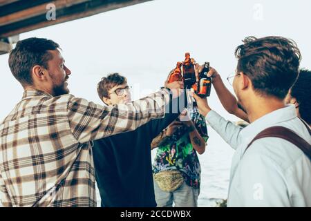 Group of friends celebrating, resting, having fun and party in summer day. Young men drinking beer, talking, laughting. Look happy and cheerful. Festive time, holiday, summertime, unity and friendship. Stock Photo