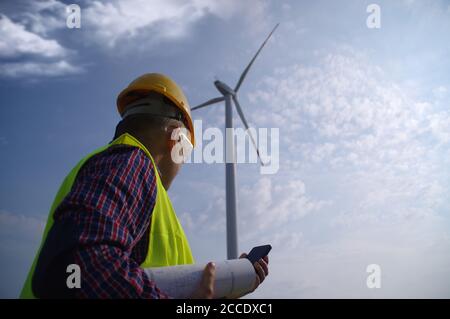 Engineer in a wind turbine. A man in a helmet supervises the operation of the electric windmills. Ecology and renewable energy sources concept. Stock Photo
