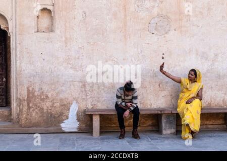 Orchha, Madhya Pradesh, India - March 2019: A young Indian female tourist wearing a yellow sari sitting on a bench and taking a selfie inside the anci Stock Photo