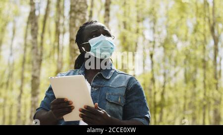 An african man with medical mask using the tablet in the forest. wireless or future technology concept. High quality photo Stock Photo