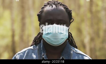 portrait shot of an african man with medical mask over the face in the park. High quality photo Stock Photo