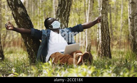 New normal. Remote work concept. African man using laptop in the nature and stretching. High quality photo Stock Photo