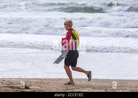 Storm Ellen brings strong wind and rough seas at Bournemouth beach, Dorset UK in August - RNLI lifeguard walking along seashore