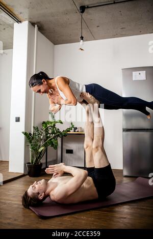 yogi caucasian couple stretching, doing exercises at home, workout on the floor. active couple lead healthy lifestyle. powerful man hold her girlfrien Stock Photo