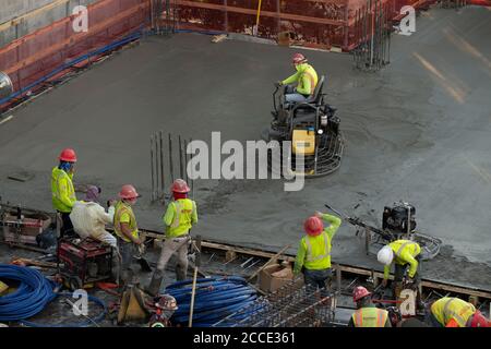 Austin, TX USA July 25, 2020: Concrete crew member operates a ride-on trowel machine during a night pour at construction site for a 53-story building in downtown Austin. Commercial construction projects continue unabated in Texas despite the nationwide COVID-19 pandemic and the state stricken with over a half million cases and 10,000-plus deaths. Stock Photo