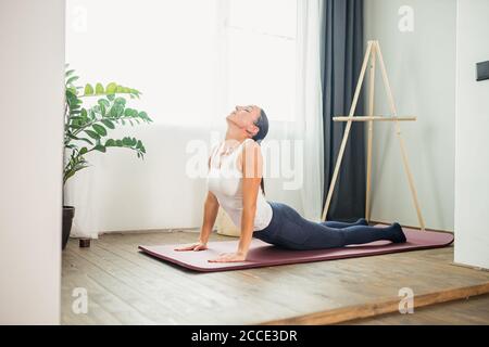 sporty caucasian woman practicing yoga, lying on the floor in Cobra pose, doing Bhujangasana exercise, female in sportswear, leggings and bra working Stock Photo