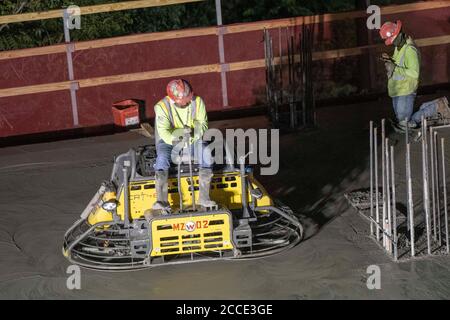 Austin, TX USA July 25, 2020: Concrete crew member operates a ride-on trowel machine during a night pour at construction site for a 53-story building in downtown Austin. Commercial construction projects continue unabated in Texas despite the nationwide COVID-19 pandemic and the state stricken with over a half million cases and 10,000-plus deaths. Stock Photo