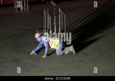 Austin, TX USA July 25, 2020: Concrete worker uses hand trowel to smooth concrete on the parking garage floor of a 53-story building during a night-time pour in downtown Austin, TX. Huge construction projects continue unabated in Texas despite the nationwide COVID-19 pandemic and the state stricken with over a half million cases and 10,000-plus deaths. Stock Photo