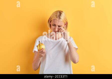 beautiful woman in white T-shirt crying while holding onion, close up portrait, studio shot. isolated yellow background, lifestyle, free time, spare t Stock Photo