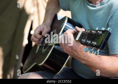Man playing classical acoustic guitar sitting near tent outdoors. Closeup of hands. Selective focus. Summer vacation concept Stock Photo