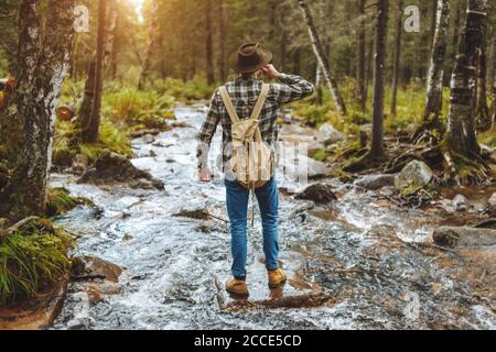 man gets pleasure from drinking cold water of stream, back view full length photo.holiday Stock Photo