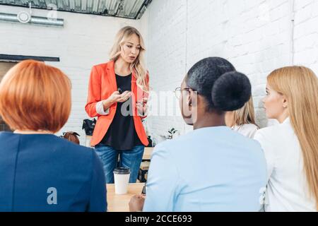 Blonde female employee make presentation for diverse employees during meeting Stock Photo