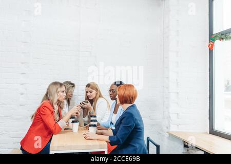Team work process. Multiracial group of young women collaborating in open space office. Red-haired mentor coach speaking to young people, teaching aud Stock Photo