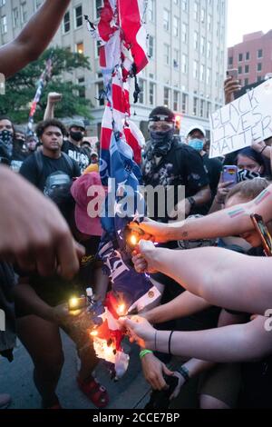 Tulsa, OK, USA. 20th Jun 2020 Protesters reach out with lighters to burn an American flag in protest of a President Donald Trump rally.