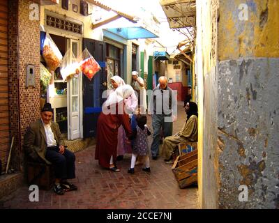 October 2005 -  The Medina is an area enclosed by walls which contains a labyrinth of souks (market places),  alleys, shops and craftspeople selling their wares . Buying always involves haggling. This photograph shows a typical street of small shops where shop owners sit outside waiting for their customers in Tangiers, Morocco Stock Photo