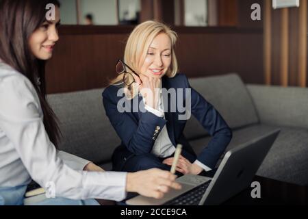 Two elegant classic business women, female partners in formal wear having conversation, planning project budget while sitting on couch in office Stock Photo