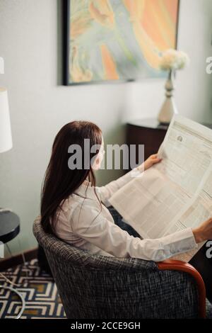 Time for morning latest news Profile side view photo of brown-haired lady sitting in a comfortable arm chair in a formal white blouse reading fresh ne Stock Photo
