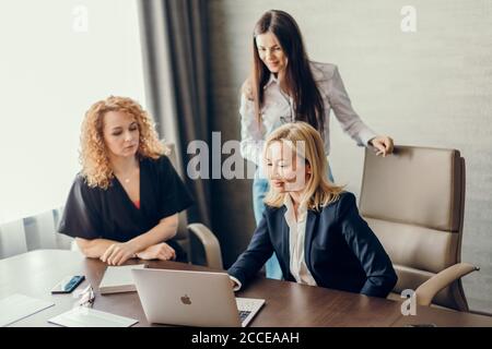 Three female fashion designers meeting in modern office interior, discussing business plans and ideas using laptop computer. Stock Photo