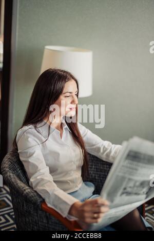 Time for morning latest news Profile side view photo of brown-haired lady sitting in a comfortable arm chair in a formal white blouse reading fresh ne Stock Photo