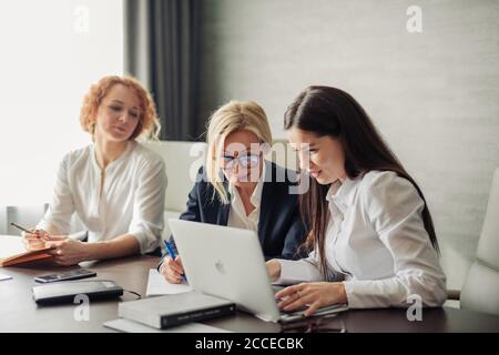 Three female fashion designers meeting in modern office interior, discussing business plans and ideas using laptop computer. Stock Photo