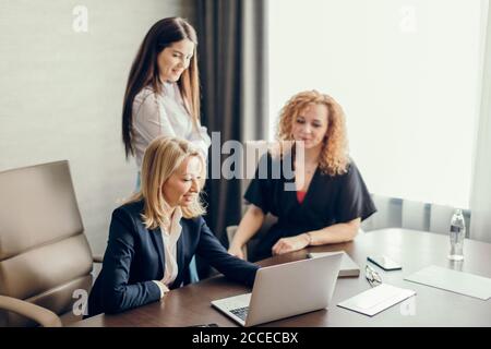Three female fashion designers meeting in modern office interior, discussing business plans and ideas using laptop computer. Stock Photo