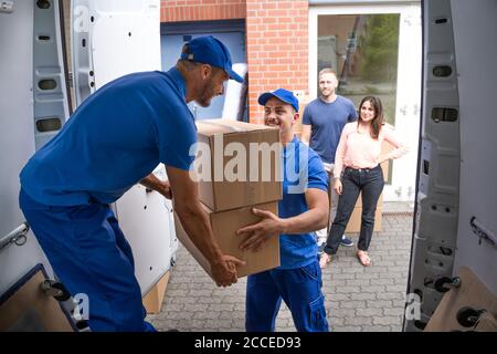 Happy Family Couple Watching Movers Unload Boxes From Truck Stock Photo