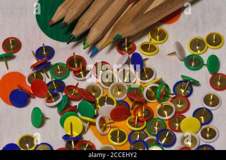 Thumbtacks and colored pencils scattered on a colored plane, horizontal image Stock Photo
