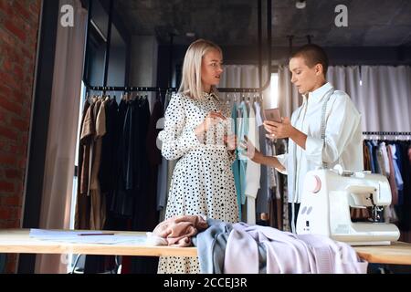 Professional dressmaker discuss with client about new dress. Creating new clothes. Blonde model and caucasian clothes designer Stock Photo
