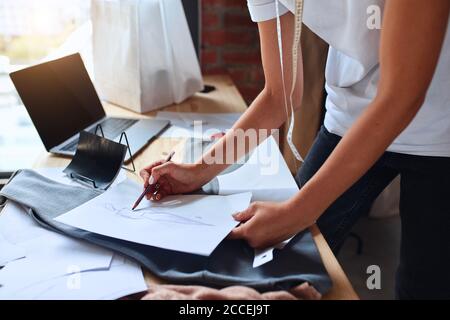 Female hand drawing dress design, using laptop in office. Creation of new clothing in studio of design Stock Photo