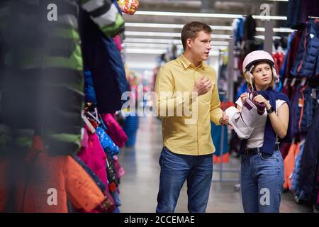 young caucasian woman wear protective helmet in sportive wear store, she came with husband to make purchase, for biking Stock Photo