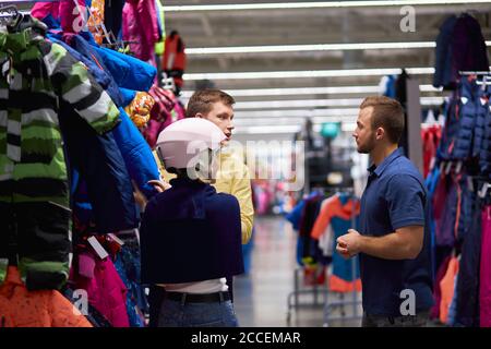 young caucasian woman wear protective helmet in sportive wear store, she came with husband to make purchase, for biking Stock Photo