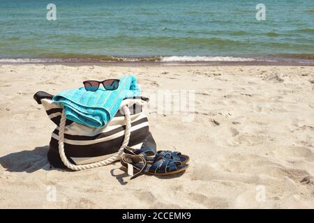 Set of personal belongings lying on the beach sand with calm sea in background in bright summer day Stock Photo