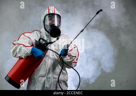 professional disinfector in an NBC personal protective equipment ppe suit, gloves, mask, cleaning isolated space with pressurized spray disinfectant w Stock Photo