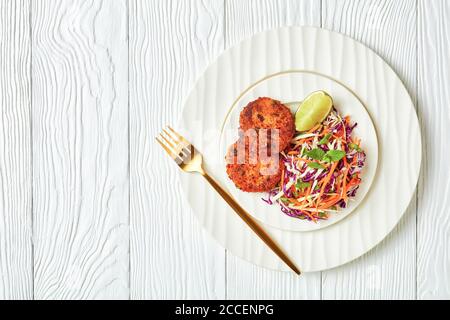 fried thai fish cakes served with coleslaw salad on a plate on a wooden table, landscape view from above, flat lay, free space Stock Photo
