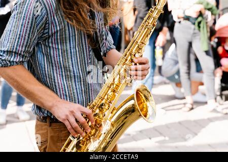 Hands of a young man with long hair playing saxophone in a crowded the street Stock Photo