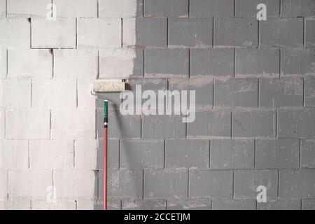 Roller is painting a rough wall of grey stones with white paint, background concept for constriction, building and renovation, copy space Stock Photo