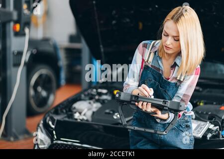 good looking blond girl checking a car by using a tablet, close up photo.diagnostic of new vehicle Stock Photo