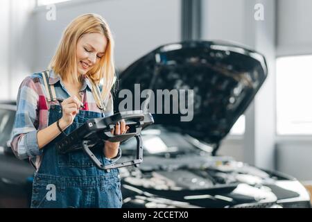 positive female mechanic showing master class at car repair shop for men. Stock Photo