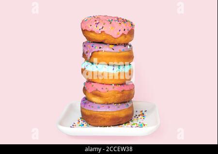 Stack of colorful donuts on a white dish on pink background. Stock Photo