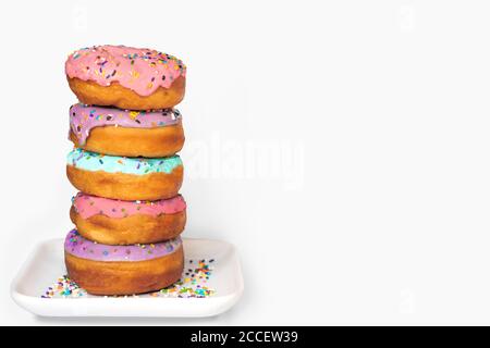 Stack of colorful donuts on a white dish on white background. Stock Photo