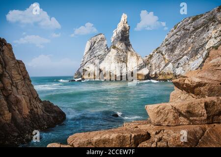 Ursa beach, Sintra, Portugal. Epic seascape of cliffs towering up from emerald green atlantic ocean. White clouds on blue sky. Summer holiday vacation Stock Photo