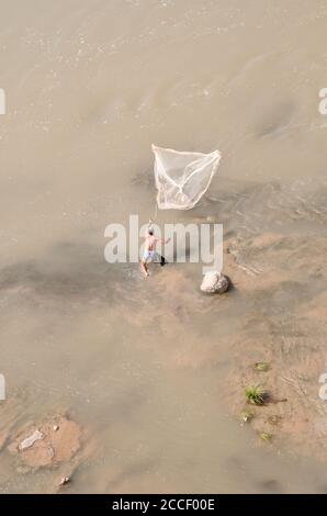 A fisherman standing in the Tigris River tries to catch fish by throwing a net, near Hasankeyf, in the eastern Anatolia region, southeastern Turkey. Stock Photo