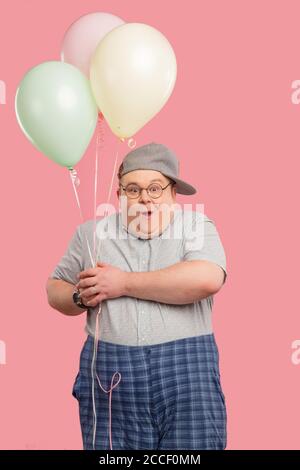 Funny adorable tubby animator, man from mini club, with vivid emotions looking cheerful, smiling happily, posing at camera, holding air balloons isola Stock Photo