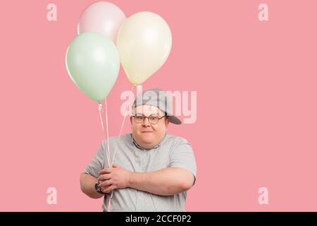 Middle aged happy father dressed in childish style looking at camera with joyful naive expression, holding colorful balloons prepares to celebrate bir Stock Photo