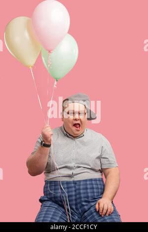 Happy funny emotional man in his 30s dressed in grey t-shirt tucked into plaid pants being overjoyed and enthusiastic about his good joke with air bal Stock Photo