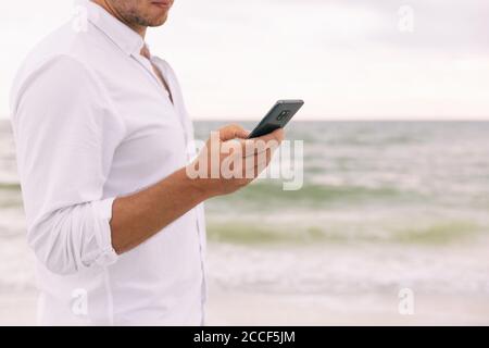 Phone business man hand holding smartphone texting sms text message online using app. Businessman on beach cellphone data on travel vacation Stock Photo
