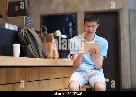 one handsome Asian young man sitting in cafe, using tablet computer. Stock Photo
