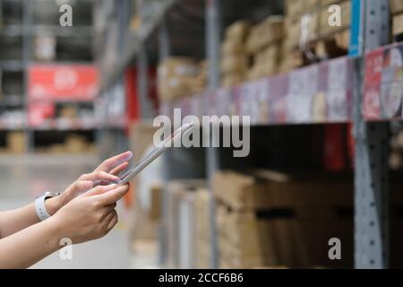 close up hands using tablet with blurred goods shelf background. warehouse, store concept Stock Photo